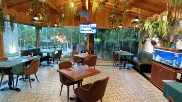 Un restaurante con techos de madera, plantas colgantes y un gran acuario. Mesas y sillas dispuestas para comer.
