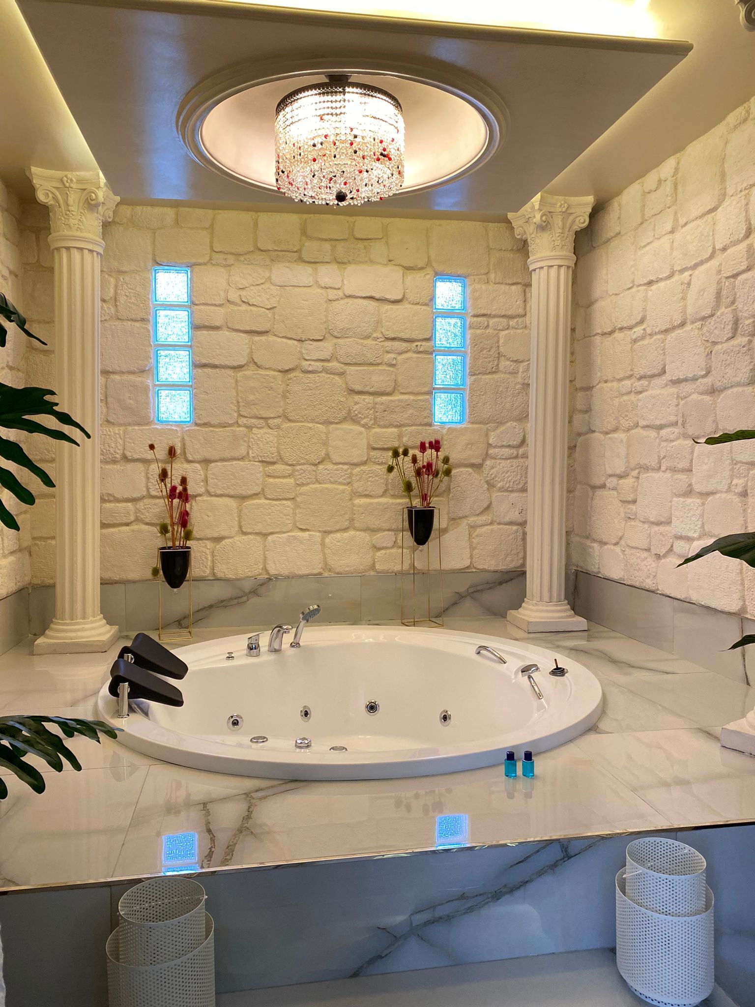 Une salle de bain luxueuse avec une grande baignoire ovale, un mur en pierre en arrière-plan et un lustre.