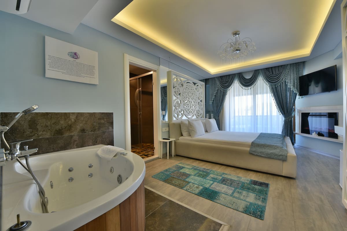 Un dormitorio moderno con una cama grande, una zona de estar, una bañera y un televisor.