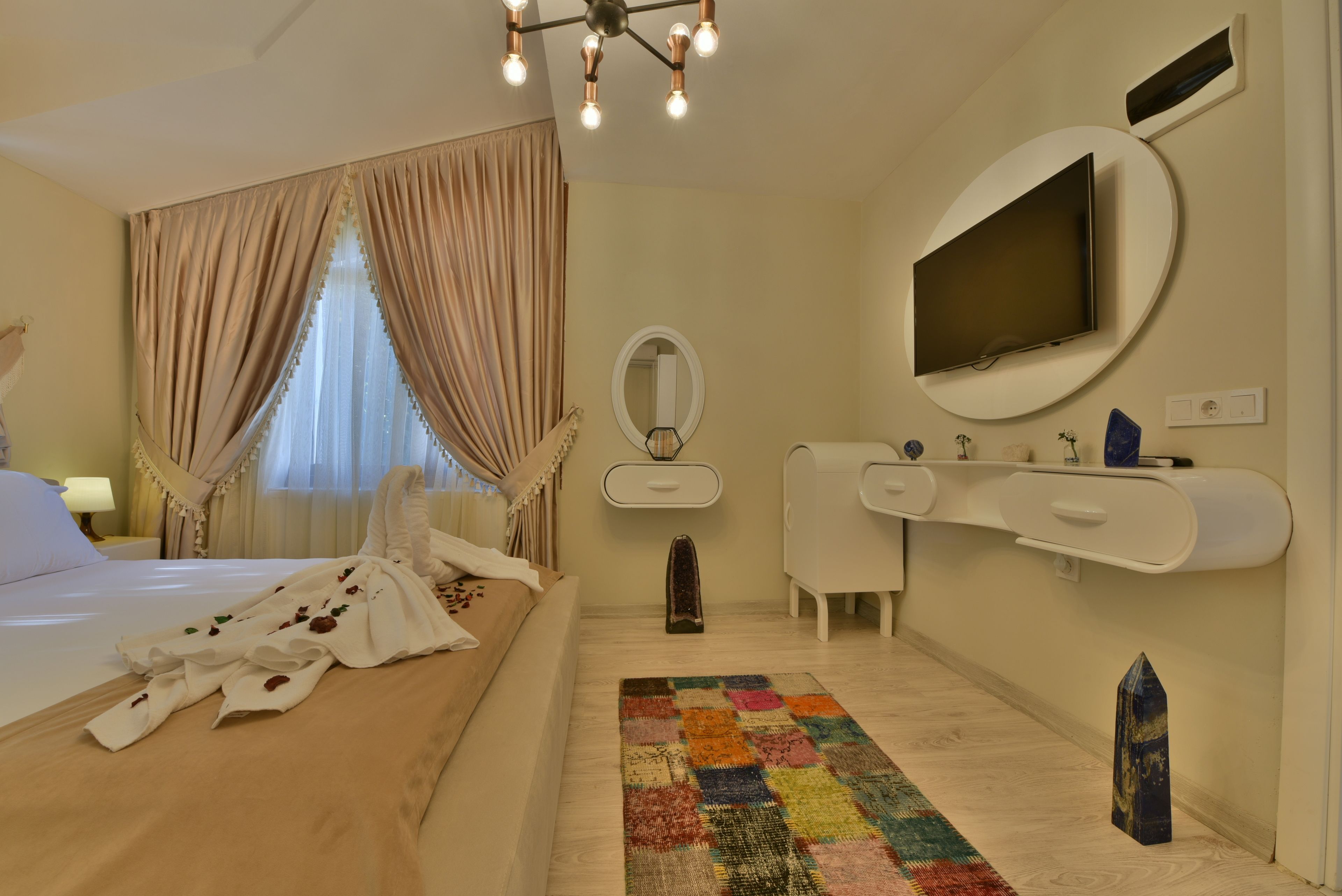 Een hotelkamer met een bed, een grote spiegel, een aan de muur bevestigde televisie, een witte dressoir en een kleurrijk vloerkleed.