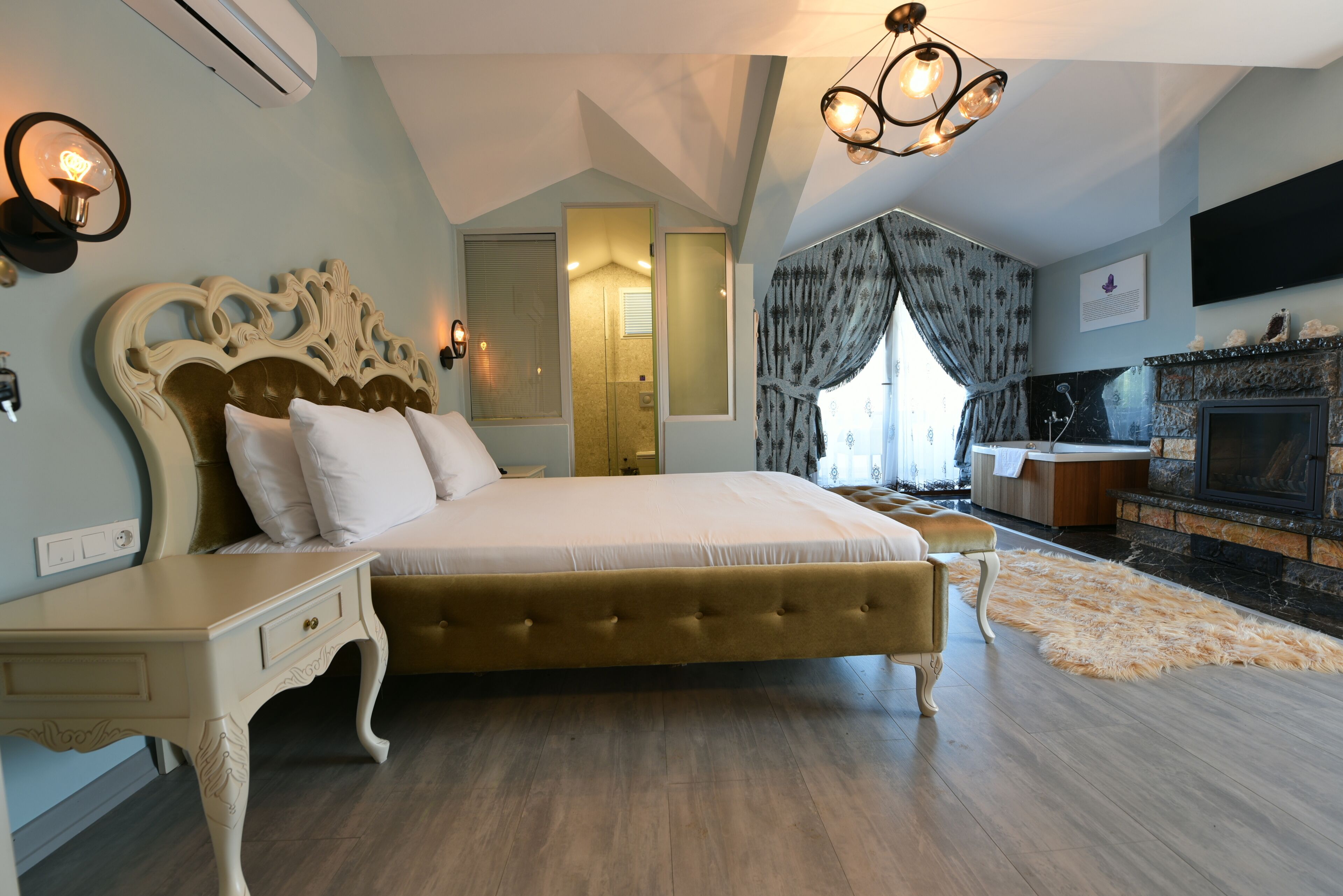 A bedroom with a large bed, a bedside table, a mirror, a fireplace, and a television.