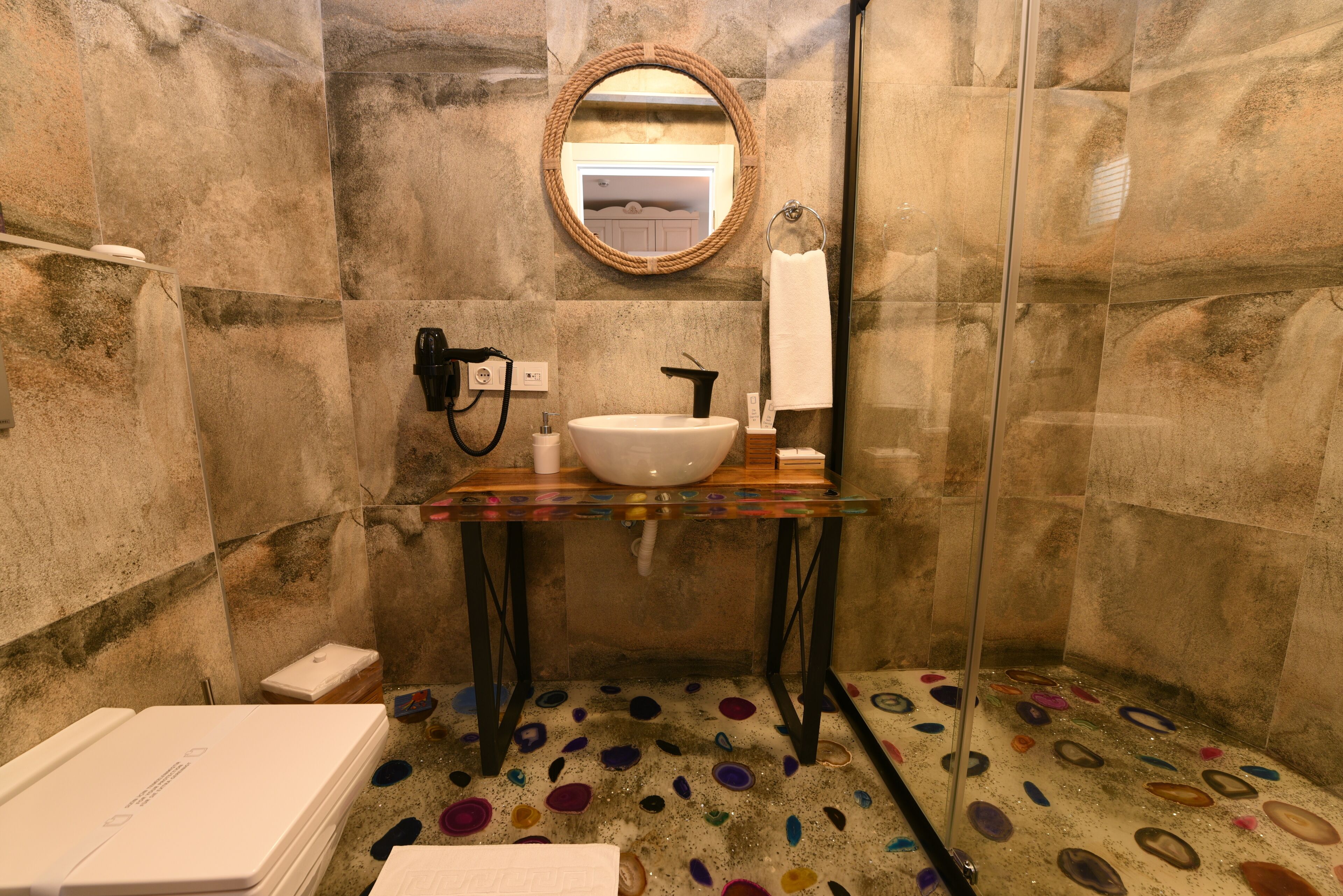 Un baño con un espejo redondo, un lavamanos blanco y una mampara de vidrio para la ducha.