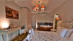A hotel room with a large bed, a bench, a desk with a lamp, a painting on the wall, and a bathroom with a bathtub and shower. - Kartepe Kosku (Kartepe)