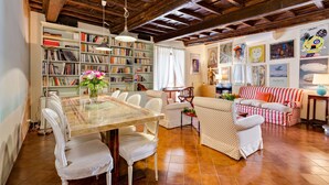 A cozy living room with a wooden ceiling, a bookshelf, a dining table with chairs, and a striped sofa. - Rome as you feel - Cappellari 35 (Rome)