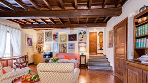 A cozy living room with patterned sofas, a wooden coffee table with fruit, and a staircase leading to a wooden door. - Rome as you feel - Cappellari 35 (Rome)
