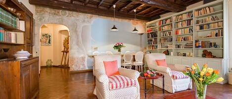 Un salón acogedor con dos sillones estampados, una mesa de centro de madera y una estantería llena de libros.