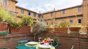 An outdoor dining area with a table set for two, surrounded by potted plants and a brick wall. - Rome as you feel - Cappellari 35 (Rome)