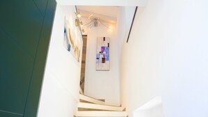 Un escalier au design moderne, menant à une pièce dont le mur est blanc et qui est éclairée par un luminaire au plafond.