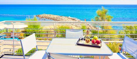 Una terrazza con un tavolo apparecchiato per mangiare, affacciata su una costa rocciosa e il mare.