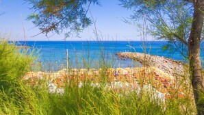 Une plage avec un rivage rocheux, une mer d’un bleu limpide et quelques personnes.