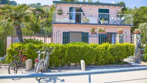 Un immeuble de deux étages doté d’un balcon, avec un vélo garé devant et une haie bien entretenue.