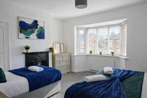 A bedroom with two beds, a dresser, a mirror, and a window with blinds. - YORK BOUTIQUE HOUSE-3 BEDROOM (YORK)