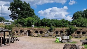 An outdoor area with stone structures resembling ancient dwellings, a picnic table, and a small shelter.