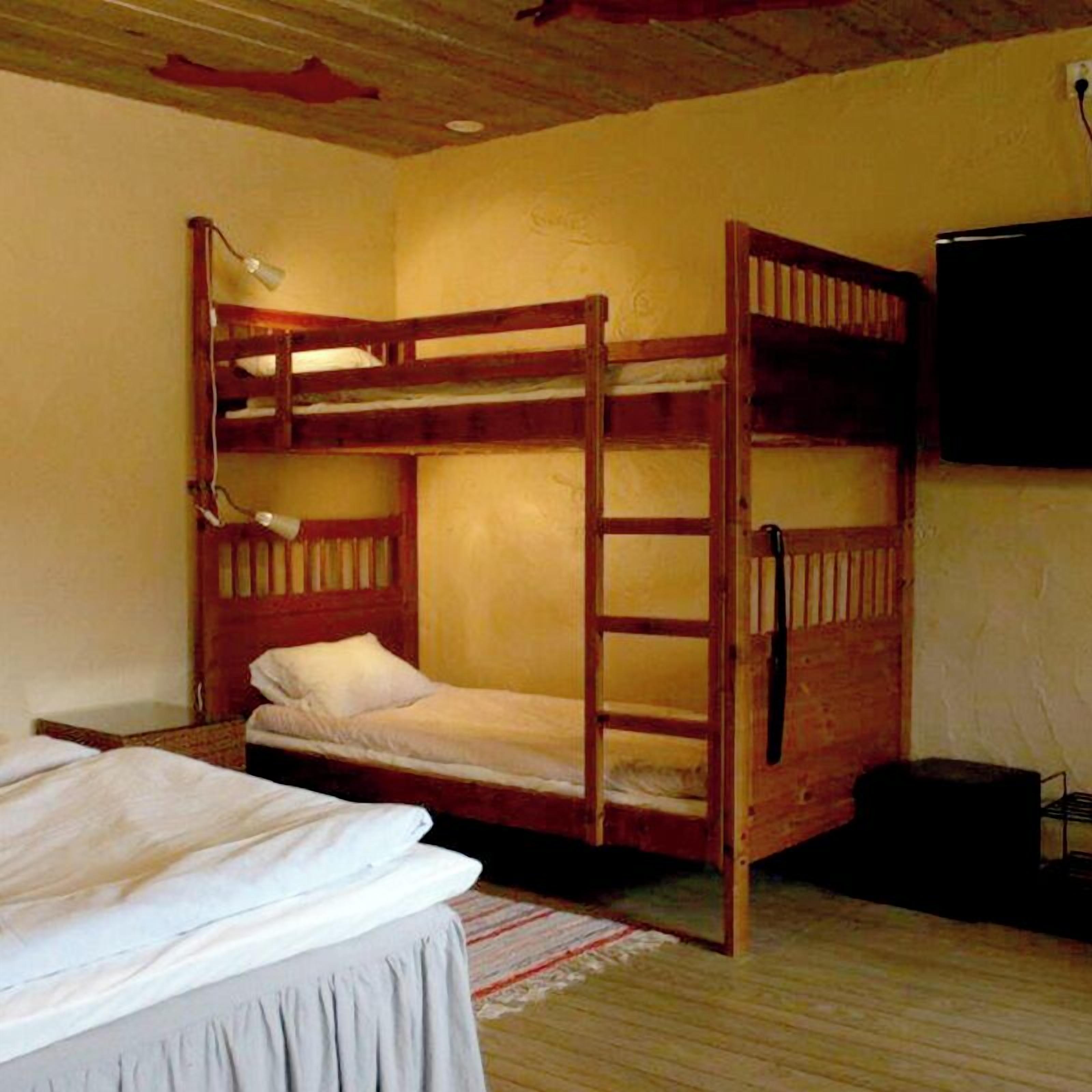 Habitación con literas, una escalera de madera, un televisor de pantalla plana en la pared y una cama con ropa de cama blanca.