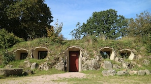 A stone structure with a central red door and three smaller arched openings, surrounded by rocks and vegetation.