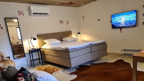 A bedroom with a bed, a desk, a chair, a mirror, and a television on the wall.