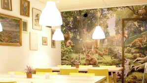A dining area with yellow chairs and a white table, decorated with framed pictures and a mural of a jungle scene.