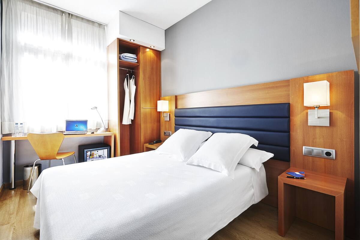 Hotellihuone, jossa on sänky, työpöytä kannettavalla tietokoneella, tuoli ja vaatekaappi.