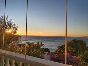 Un balcon offrant une vue sur la mer et sur la terre, au loin, au coucher du soleil.