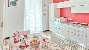 A kitchen with white cabinets, a red wall, and a window with curtains. There is a table with a coffee maker, cups, and a basket of oranges. - Via Dante Vacanze - large apartment for 4 people, 200 meters from the beach, in Levanto (Levanto)