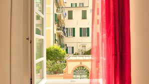 A view from a window with a red curtain, overlooking a building with balconies and a small archway. - Via Dante Vacanze - large apartment for 4 people, 200 meters from the beach, in Levanto (Levanto)