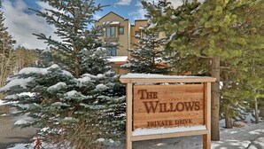 A wooden sign reading "The Willows Private Drive" in a snowy landscape with evergreen trees and a building in the background. - 102 Willows Way 3 Bedroom Townhouse by RedAwning (Winter Park)