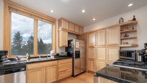 A modern kitchen with wooden cabinets, stainless steel appliances, a large window, and a view of trees. - 102 Willows Way 3 Bedroom Townhouse by RedAwning (Winter Park)