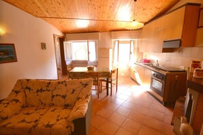 Una sala de estar acogedora con un sofá estampado, un comedor con mesa y sillas, y una cocina con armarios de madera y electrodomésticos.
