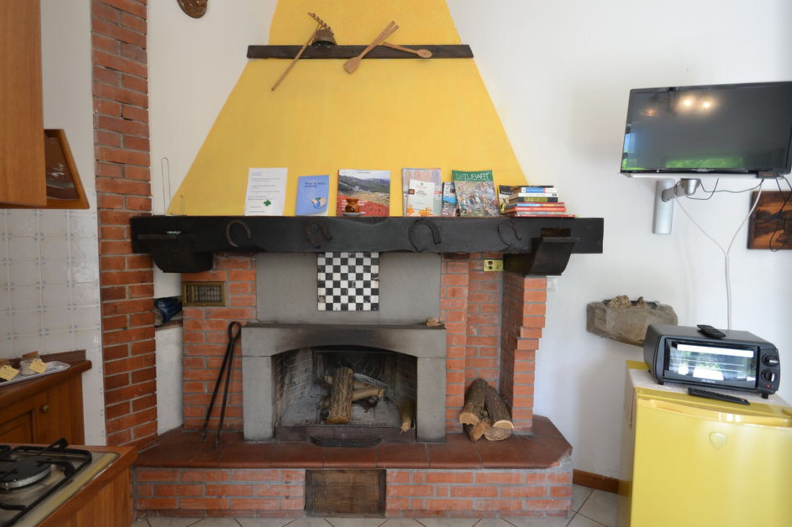 Een keuken met een bakstenen open haard, een gele wand, en een televisie erboven.