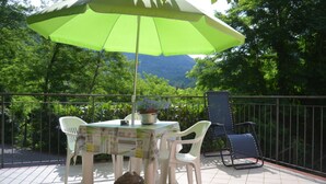 Um pátio com uma mesa e cadeiras, um guarda-sol verde e vista para uma montanha arborizada.