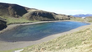 Um lago límpido rodeado por colinas gramadas e montanhas.