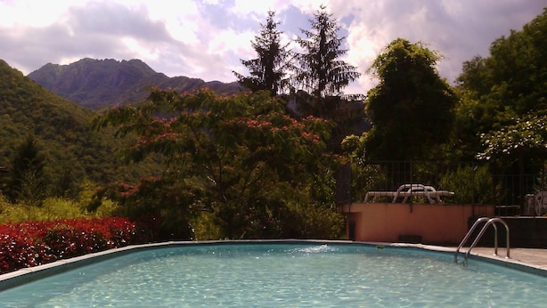 Uma piscina com água cristalina, rodeada por vegetação exuberante e montanhas ao fundo.
