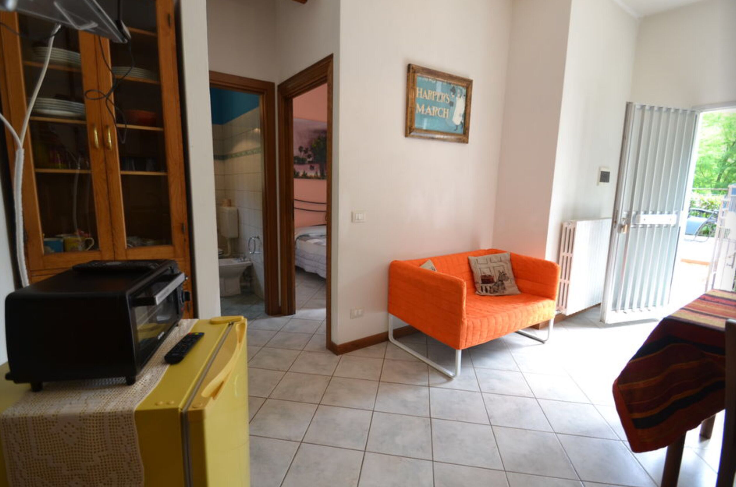 A room with a kitchenette, a sofa, a dining table, and a view through an open door.