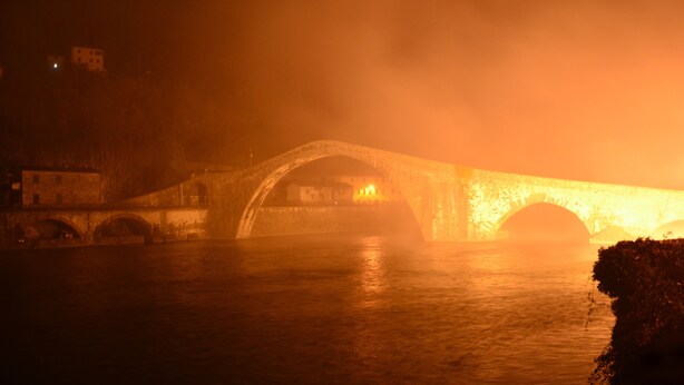 Een stenen brug over water, 's nachts verlicht.