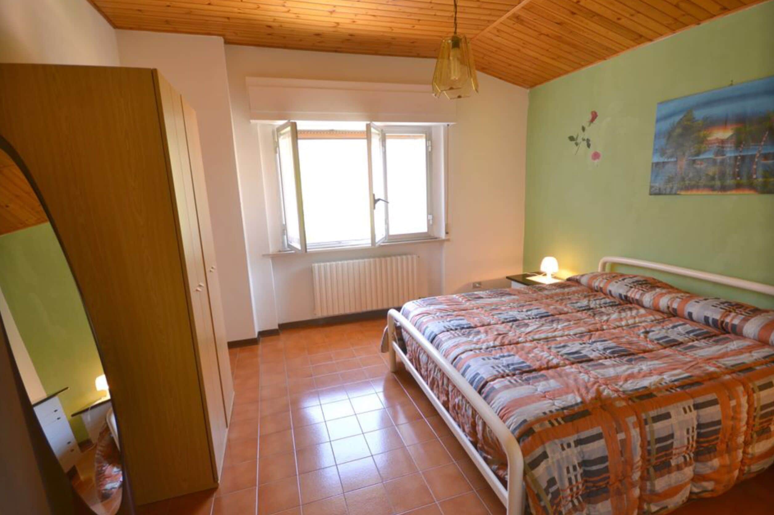 Un dormitorio con cama, ventana, radiador y techo de madera.