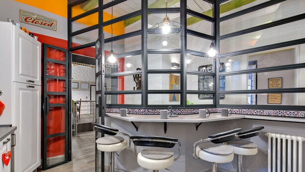 A modern kitchen with a bar area, featuring a large window, a refrigerator, and three bar stools. - Rome as you feel - Design at Colosseum (Rome)