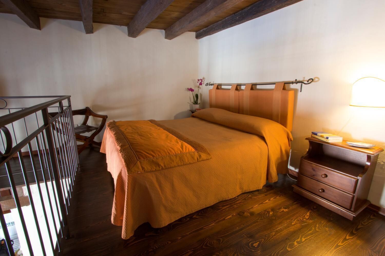 Un dormitorio con cama de madera, una mesita de noche, una silla y barandilla de balcón.