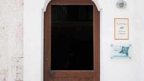 A wooden door with a small window above it, a wall-mounted light, and a plaque with text. - Le Case di Sottovento (Mola di Bari)