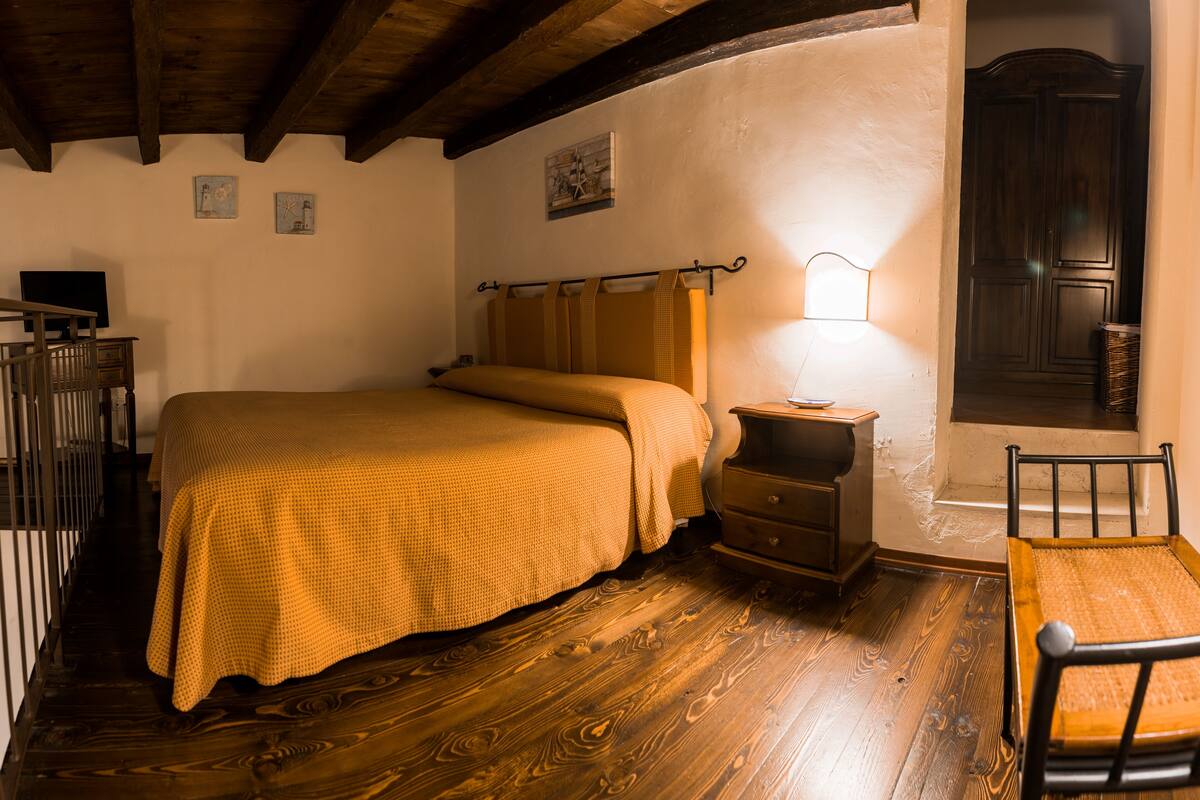 A bedroom with a wooden bed, a nightstand, a lamp, and a chair.