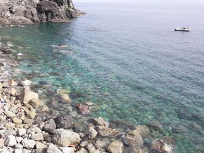 Una costa rocosa con agua cristalina, un barco a lo lejos y una persona nadando.