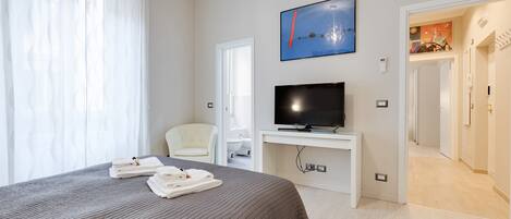 A hotel room with a bed, a TV, a chair, and a bathroom visible through an open door.