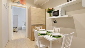 Un comedor con una mesa blanca dispuesta para cuatro personas, un microondas en un estante y un armario de madera.