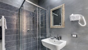 Un baño moderno con ducha de vidrio, un lavamanos blanco y un espejo con un marco decorativo.