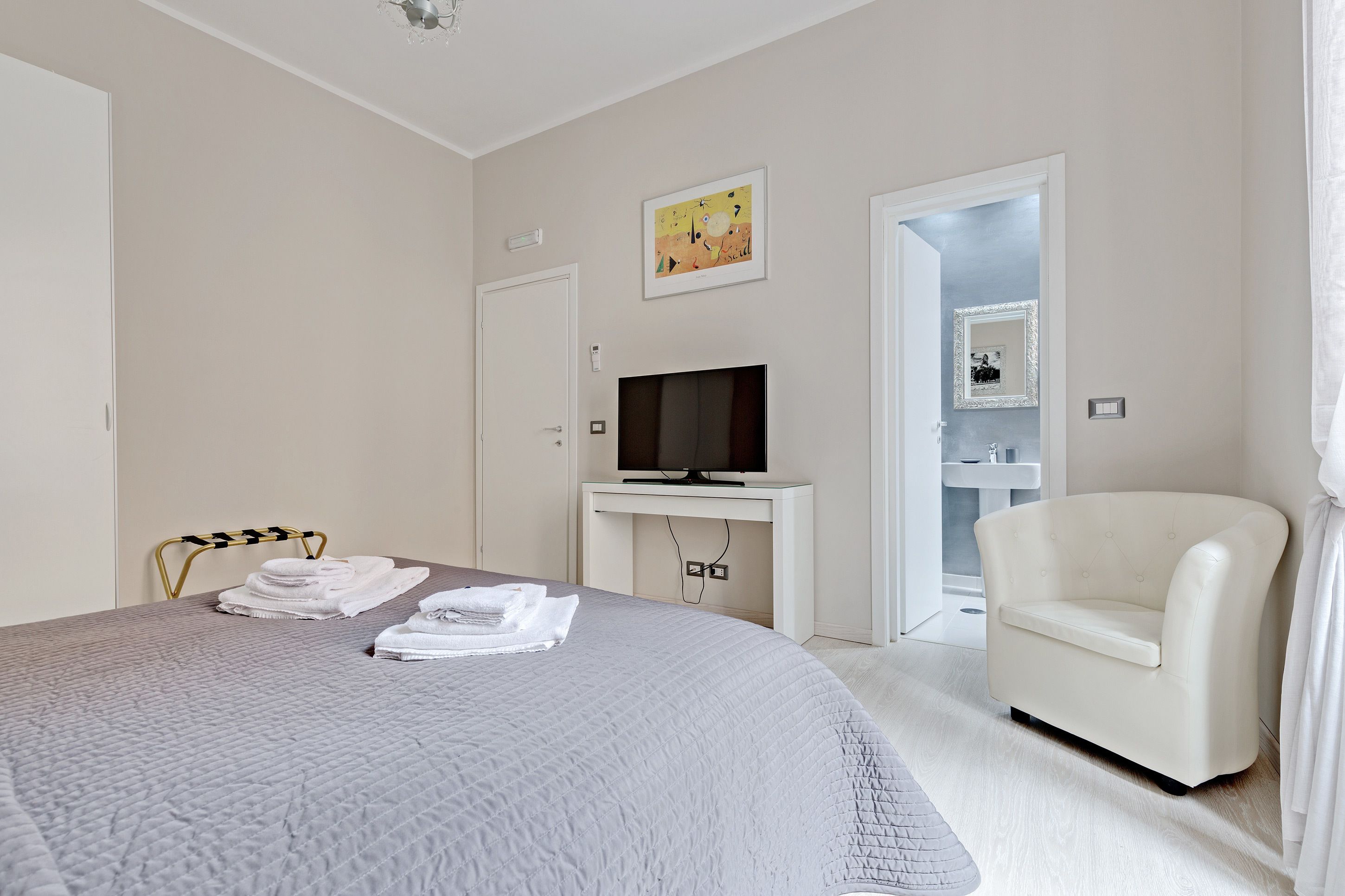 Une chambre d’hôtel avec un lit, une télévision, une chaise et une salle de bain visible à travers une porte ouverte.
