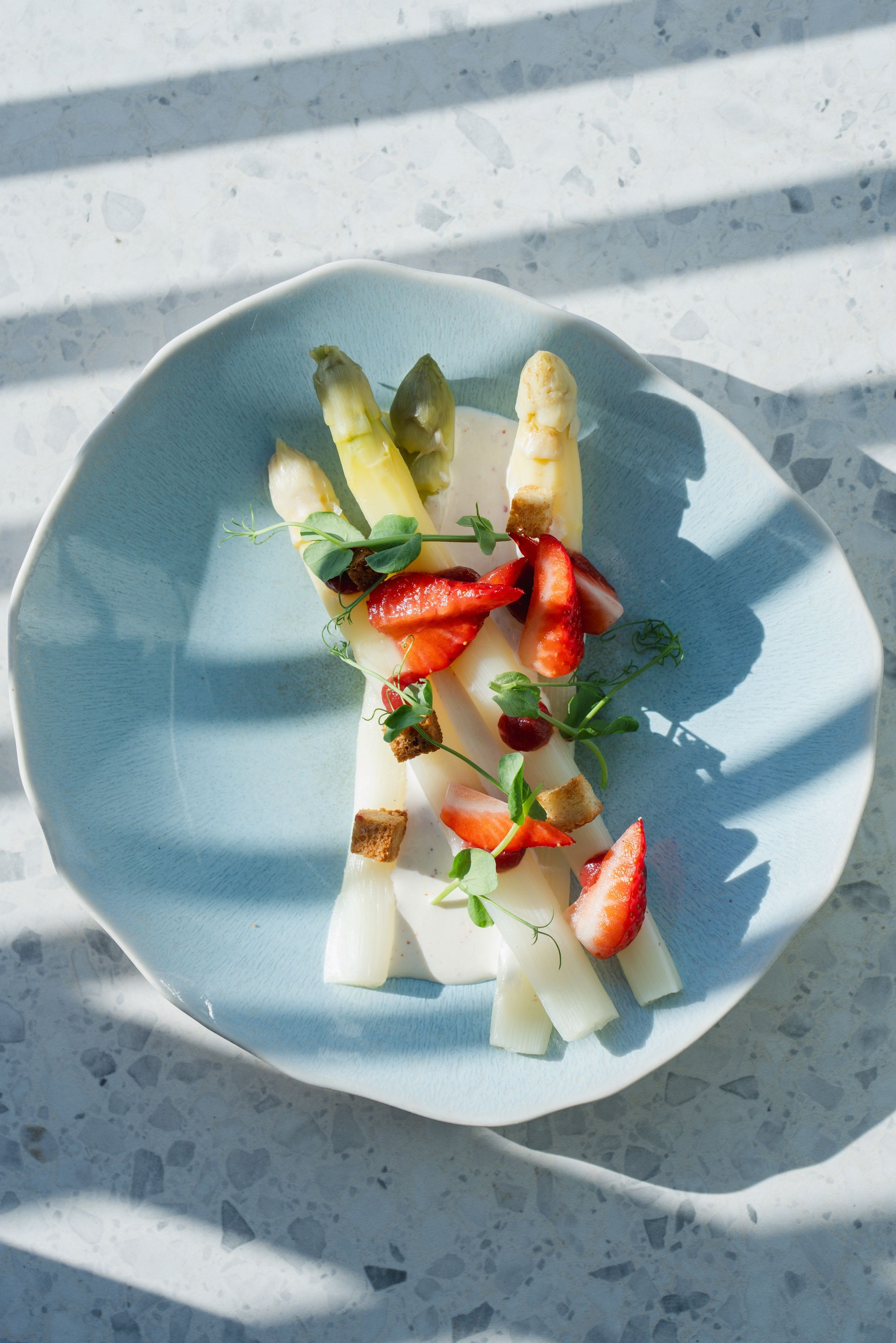 Un plato con espárragos, fresas y una pequeña guarnición sobre un plato azul.