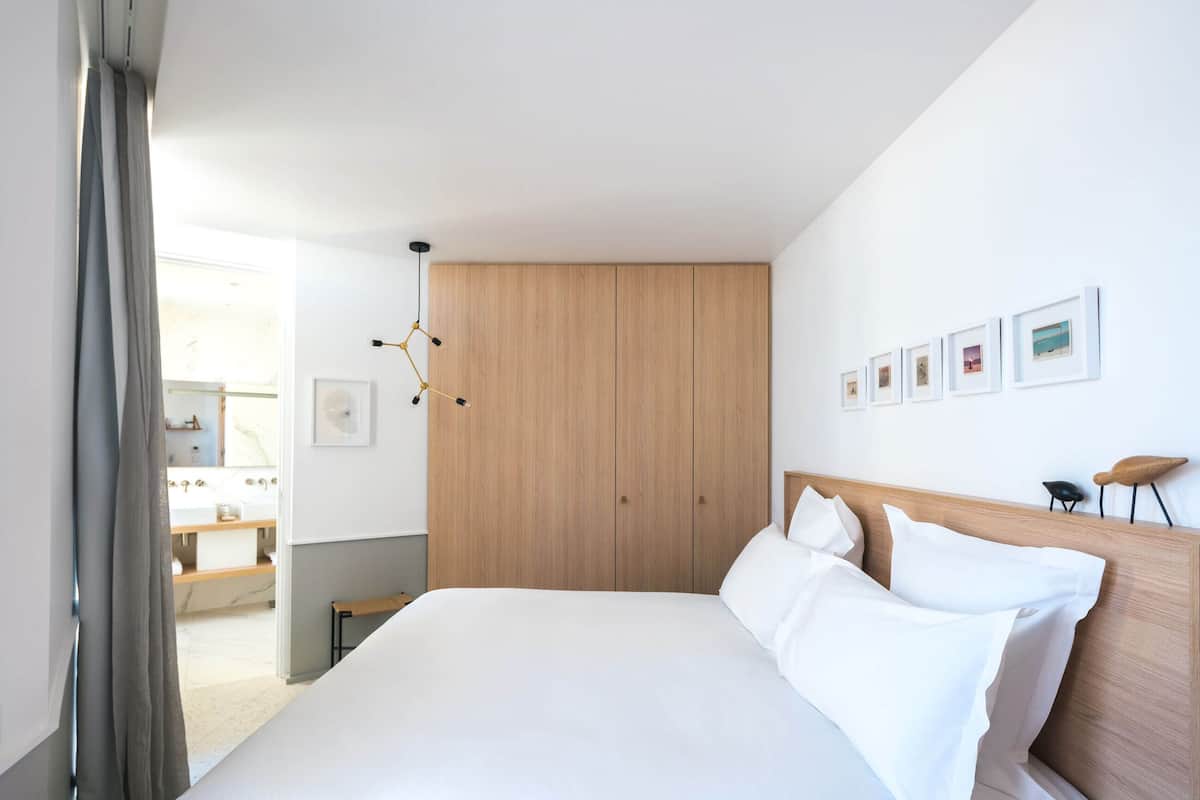 A modern hotel room with a large bed, wooden wardrobe, and a series of framed pictures on the wall.