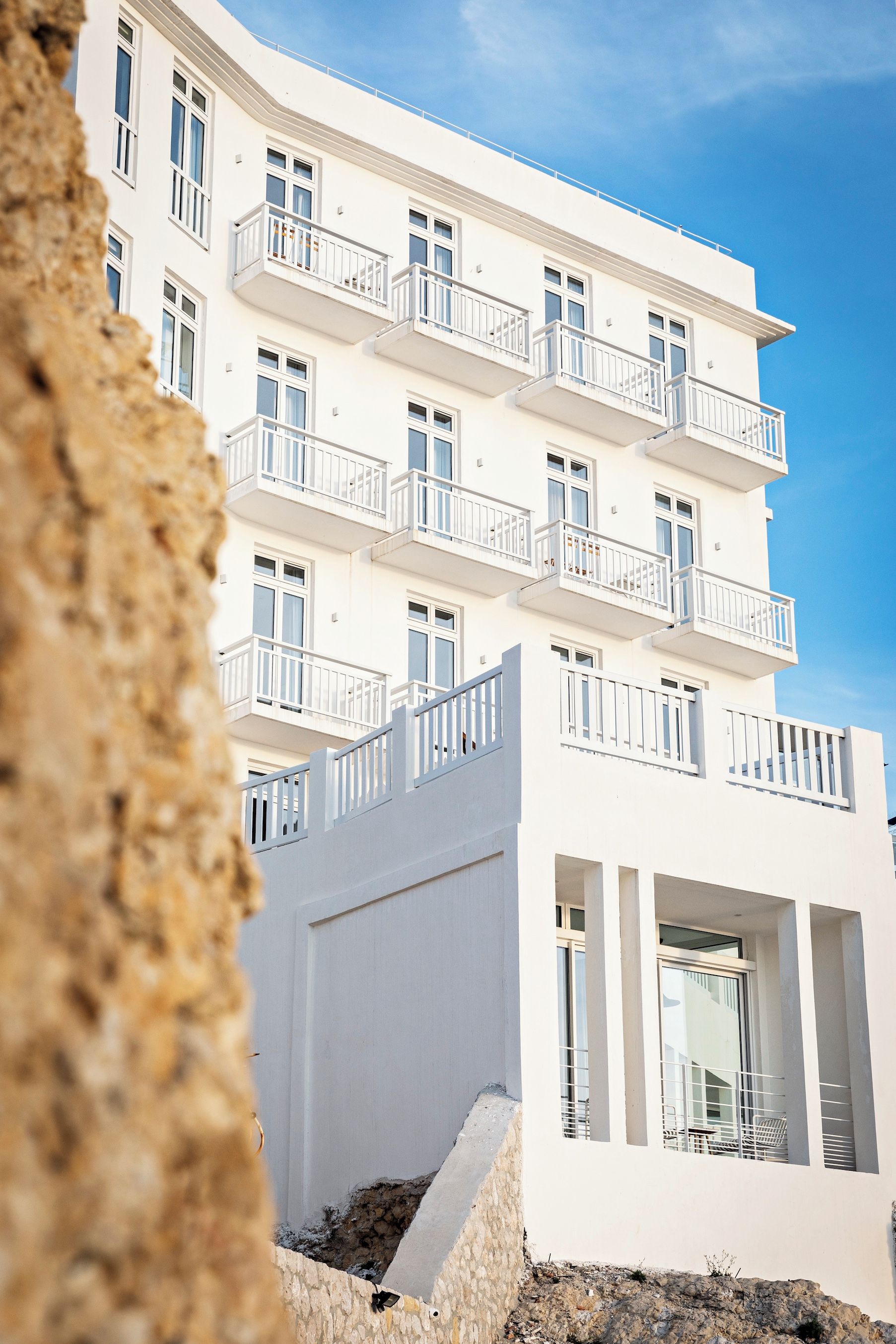 Un immeuble à plusieurs étages doté de balcons, un mur de pierre au premier plan et un ciel dégagé.