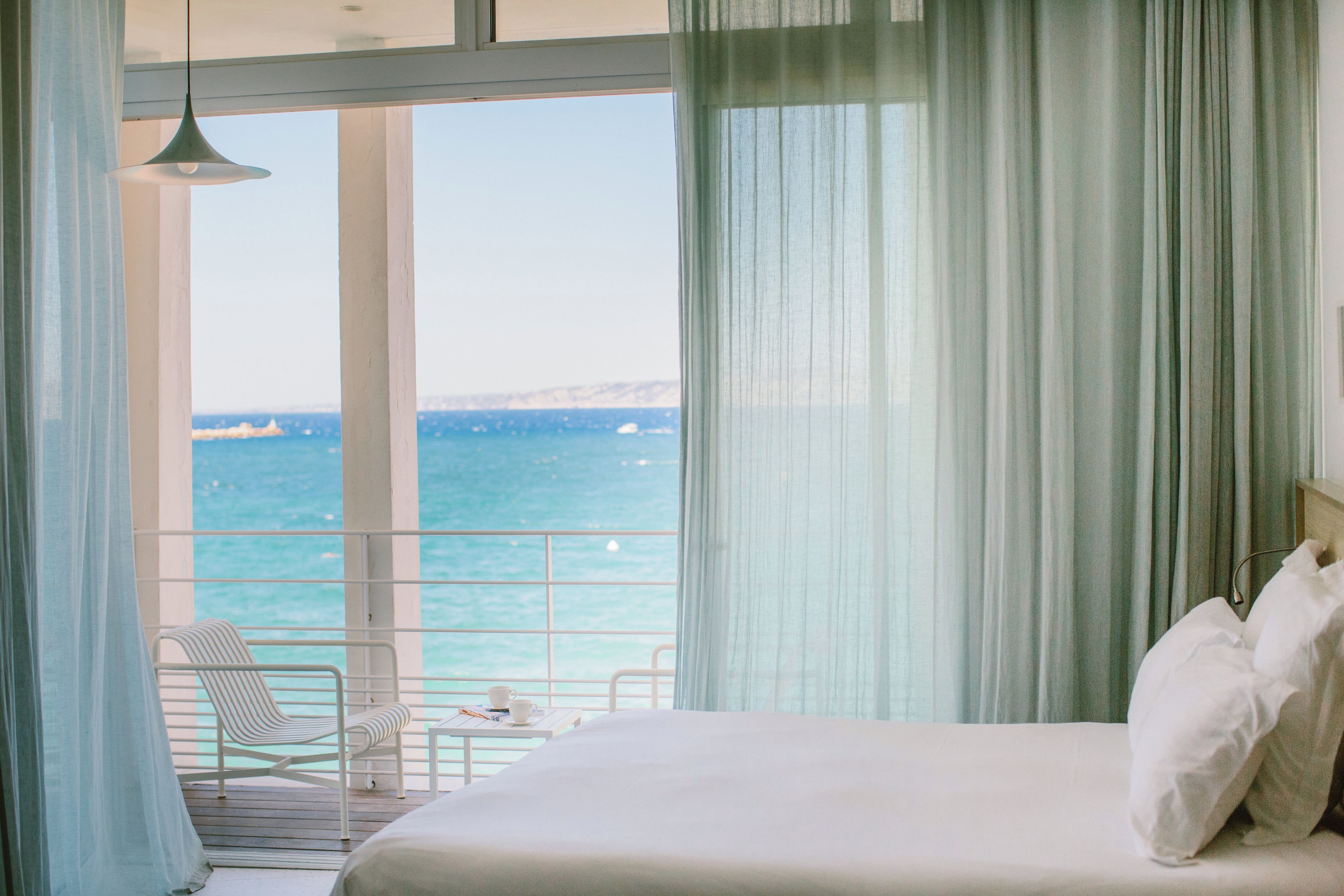 Een hotelkamer met een bed, een stoel, een tafel en uitzicht op zee.