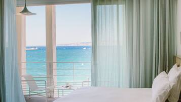 Een hotelkamer met een bed, een stoel, een tafel en uitzicht op zee.
