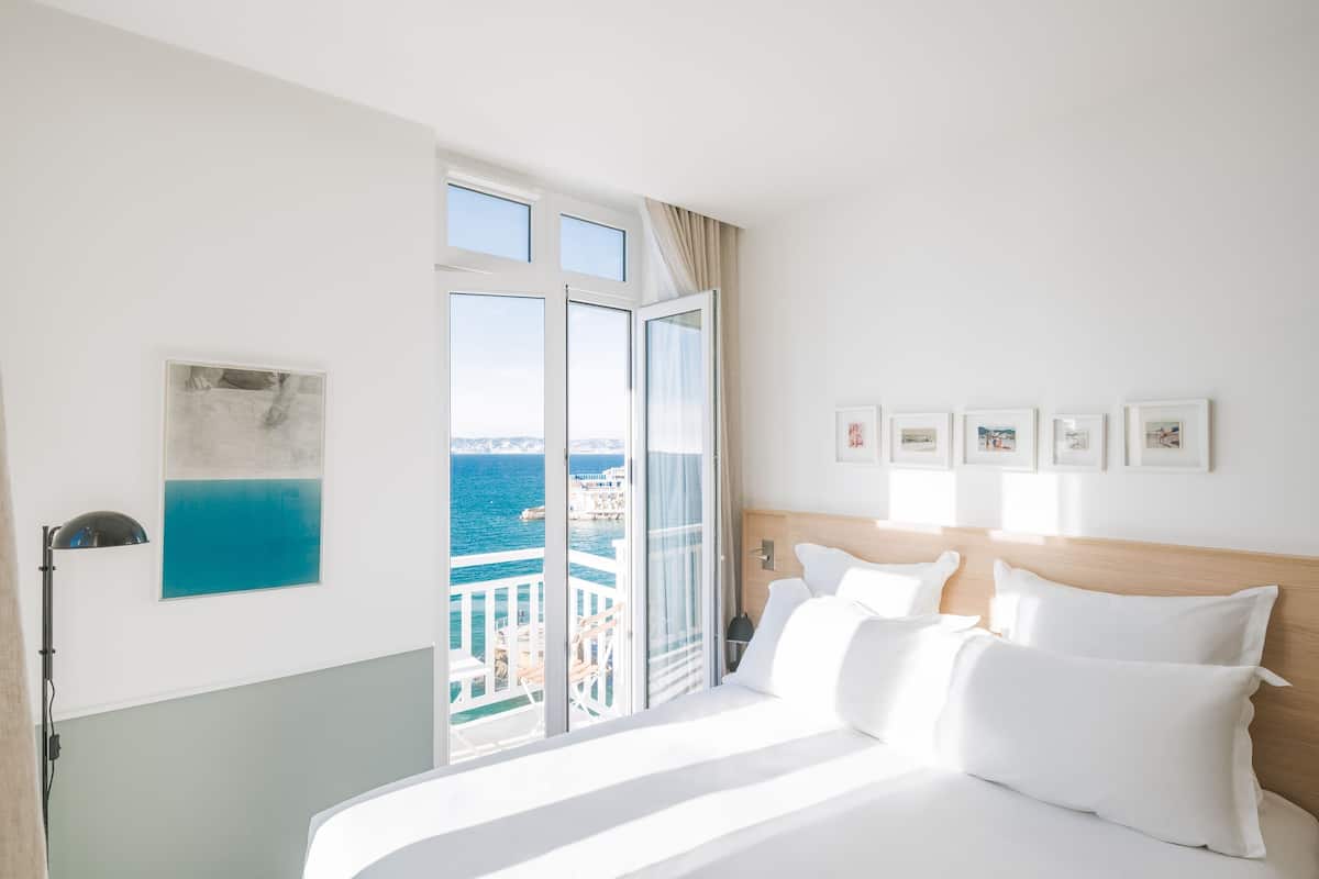 A hotel room with a large bed, a view of the sea, and a balcony.